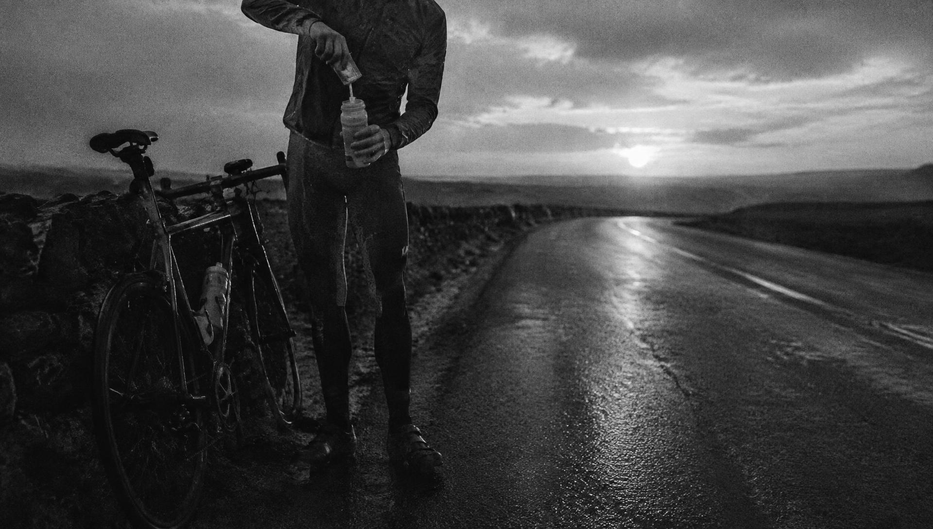 Cyclist mixing a drink bottle on a wet road at dawn