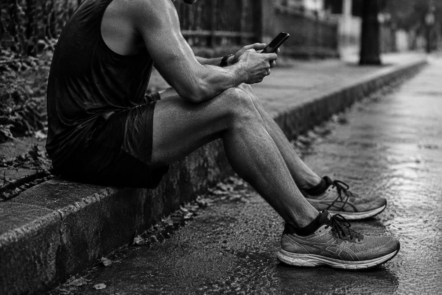 Runner on a kerb scrolling a phone after a run
